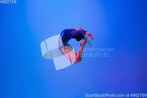 Image of Young flexible girl isolated on blue studio background. Young female model practicing artistic gymnastics. Exercises for flexibility, balance.