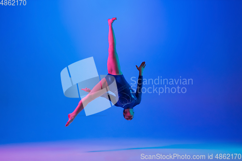 Image of Young flexible girl isolated on blue studio background. Young female model practicing artistic gymnastics. Exercises for flexibility, balance.