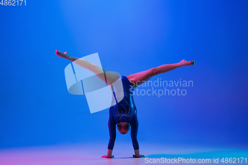 Image of Young flexible girl isolated on blue studio background. Young female model practicing artistic gymnastics. Exercises for flexibility, balance.