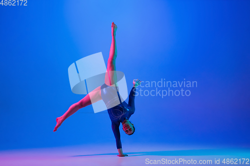 Image of Young flexible girl isolated on blue studio background. Young female model practicing artistic gymnastics. Exercises for flexibility, balance.