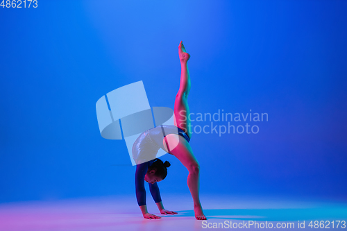 Image of Young flexible girl isolated on blue studio background. Young female model practicing artistic gymnastics. Exercises for flexibility, balance.