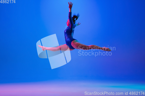 Image of Young flexible girl isolated on blue studio background. Young female model practicing artistic gymnastics. Exercises for flexibility, balance.