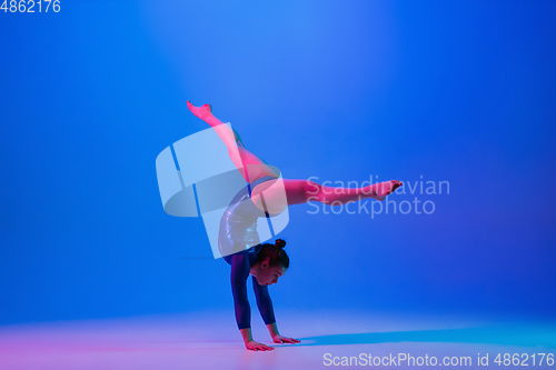 Image of Young flexible girl isolated on blue studio background. Young female model practicing artistic gymnastics. Exercises for flexibility, balance.