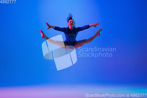 Image of Young flexible girl isolated on blue studio background. Young female model practicing artistic gymnastics. Exercises for flexibility, balance.