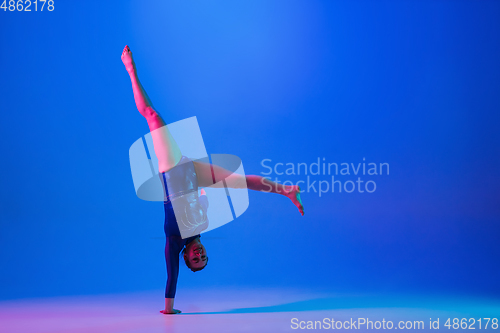 Image of Young flexible girl isolated on blue studio background. Young female model practicing artistic gymnastics. Exercises for flexibility, balance.