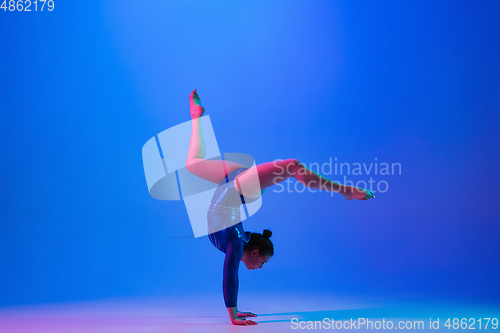 Image of Young flexible girl isolated on blue studio background. Young female model practicing artistic gymnastics. Exercises for flexibility, balance.