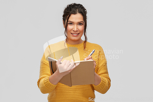 Image of happy young woman writing to diary or notebook