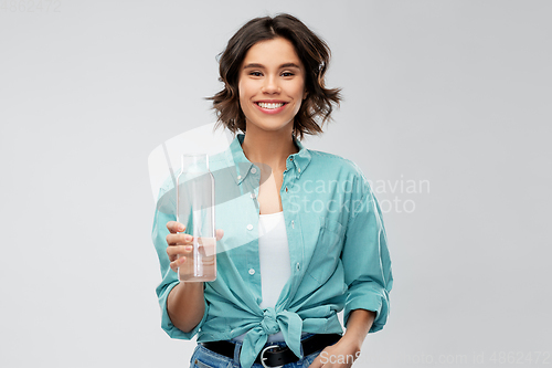 Image of smiling young woman holding water in glass bottle