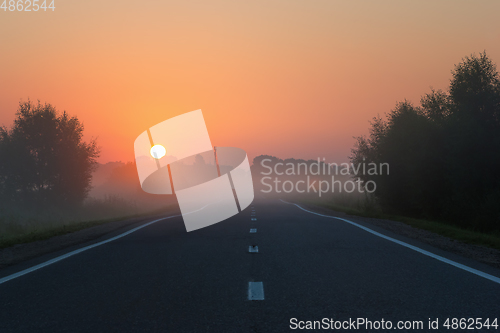 Image of Empty Road Leading to Golden Sunrise on Foggy Morning