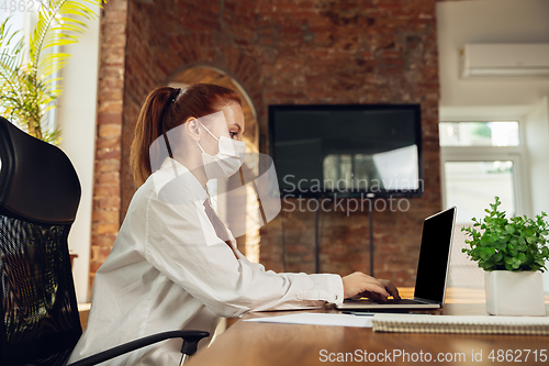 Image of Woman working in office alone during coronavirus or COVID-19 quarantine, wearing face mask