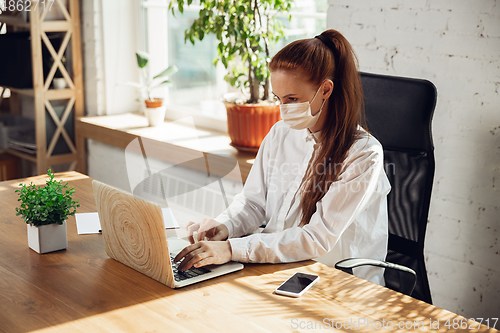 Image of Woman working in office alone during coronavirus or COVID-19 quarantine, wearing face mask