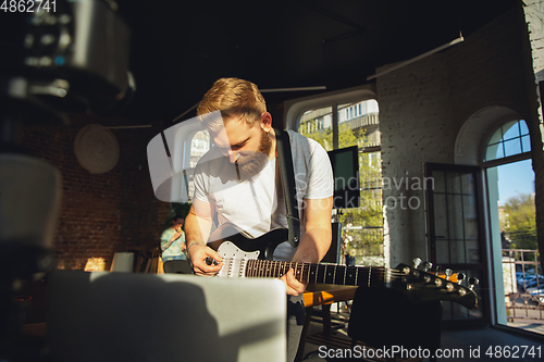 Image of Caucasian musician playing guitar during online concert at home isolated and quarantined, impressive improvising in sunlight