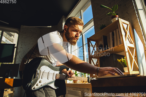 Image of Caucasian musician playing guitar during online concert at home isolated and quarantined, tuning the stream