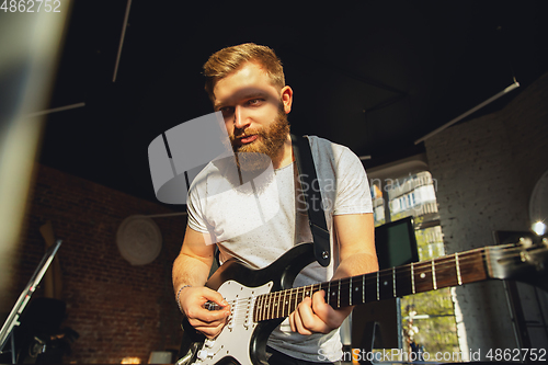 Image of Caucasian musician playing guitar during online concert at home isolated and quarantined, impressive improvising in sunlight