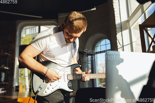 Image of Caucasian musician playing guitar during online concert at home isolated and quarantined, impressive improvising in sunlight
