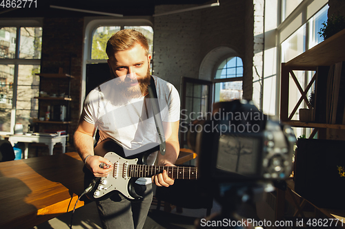 Image of Caucasian musician playing guitar during online concert at home isolated and quarantined, impressive improvising in sunlight