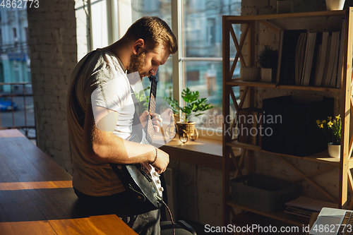 Image of Caucasian musician playing guitar during online concert at home isolated and quarantined, impressive improvising in sunlight