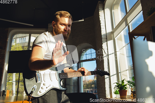 Image of Caucasian musician playing guitar during online concert at home isolated and quarantined, greeting