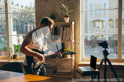 Image of Caucasian musician playing guitar during online concert at home isolated and quarantined, impressive improvising