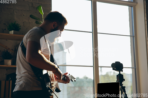 Image of Caucasian musician playing guitar during online concert at home isolated and quarantined, impressive improvising