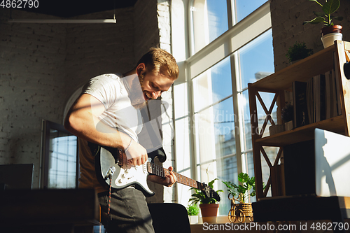 Image of Caucasian musician playing guitar during online concert at home isolated and quarantined, impressive improvising in sunlight