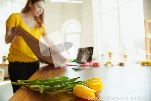 Image of Florist at work: woman shows how to make bouquet with tulips, working at home concept, using coverage paper