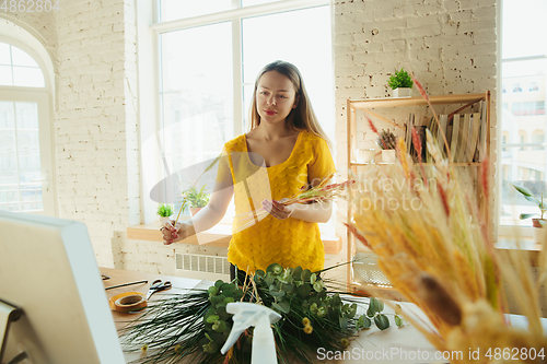 Image of Florist at work: woman shows how to make bouquet, working at home concept, choosing plants for composition