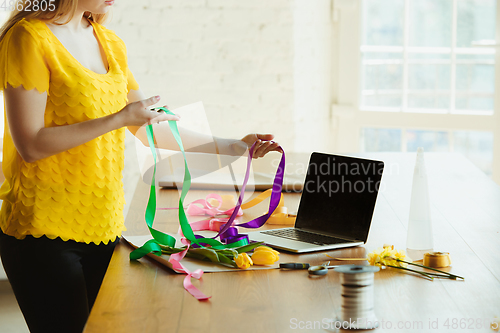 Image of Florist at work: woman shows how to make bouquet with tulips, working at home concept, using ribbons