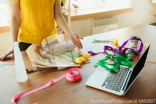 Image of Florist at work: woman shows how to make bouquet with tulips, working at home concept, choosing decoration