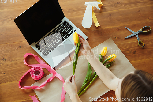 Image of Florist at work: woman shows how to make bouquet with tulips, working at home concept, top view