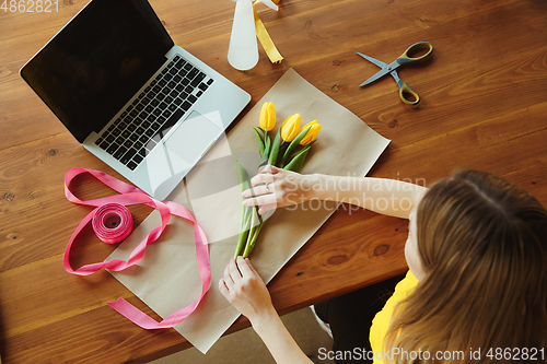 Image of Florist at work: woman shows how to make bouquet with tulips, working at home concept, top view