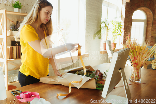 Image of Florist at work: woman shows how to make bouquet, working at home concept, using paper coverage