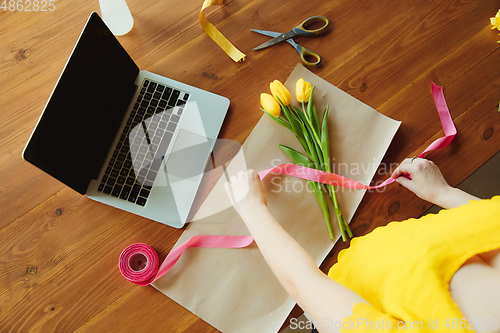 Image of Florist at work: woman shows how to make bouquet with tulips, working at home concept, top view