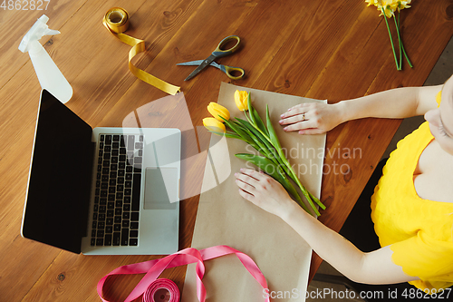 Image of Florist at work: woman shows how to make bouquet with tulips, working at home concept, top view