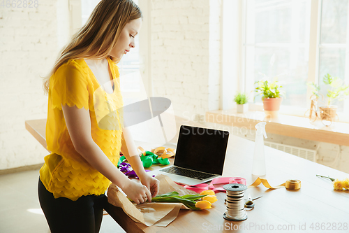 Image of Florist at work: woman shows how to make bouquet with tulips, working at home concept, preparing flowers