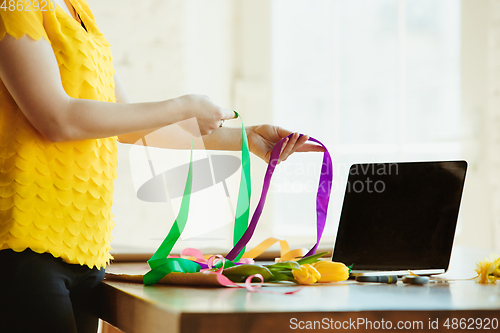 Image of Florist at work: woman shows how to make bouquet with tulips, working at home concept, using ribbons