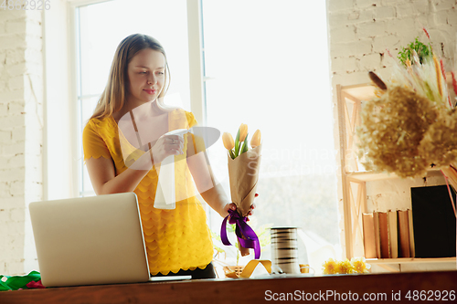 Image of Florist at work: woman shows how to make bouquet with tulips, working at home concept, using spray