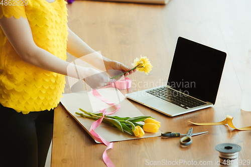 Image of Florist at work: woman shows how to make bouquet with tulips, working at home concept, adds daffodils