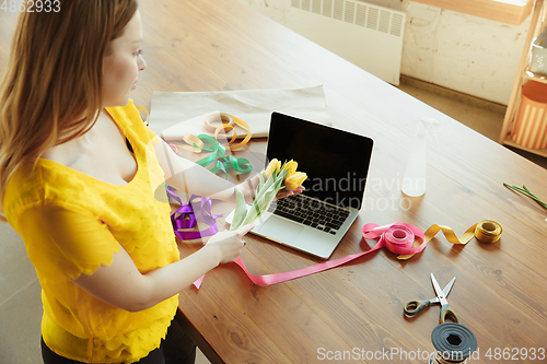 Image of Florist at work: woman shows how to make bouquet with tulips, working at home concept, preparing flowers