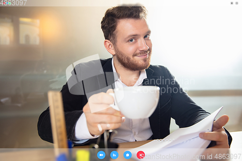Image of Young man talking, working in videoconference with co-workers at office or living room. Online business, education during quarantine.