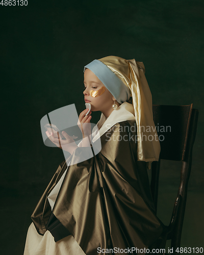 Image of Medieval little girl as a lady with a pearl earring on dark studio background. Concept of comparison of eras, childhood. Stylish creative design, art vision, new look of artwork.