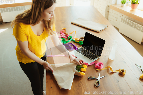 Image of Florist at work: woman shows how to make bouquet with tulips, working at home concept, using coverage paper