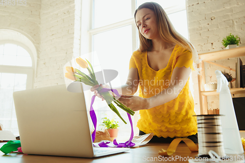 Image of Florist at work: woman shows how to make bouquet with tulips, working at home concept, preparing flowers