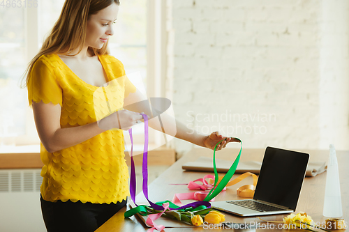 Image of Florist at work: woman shows how to make bouquet with tulips, working at home concept, using ribbons