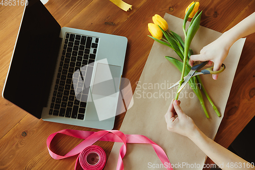 Image of Florist at work: woman shows how to make bouquet with tulips, working at home concept, top view