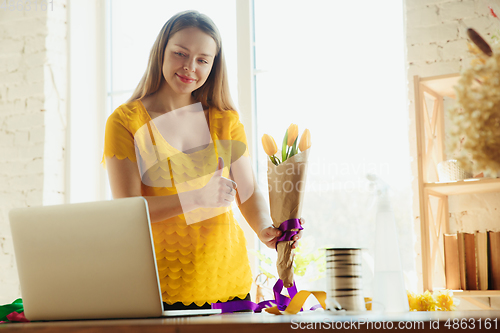 Image of Florist at work: woman shows how to make bouquet with tulips, working at home concept, thumb up