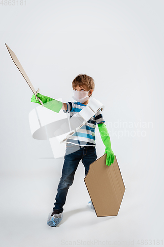 Image of Little caucasian boy as a warrior in fight with coronavirus pandemic, with a shield, a sword and a toilet paper bandoleer, attacking