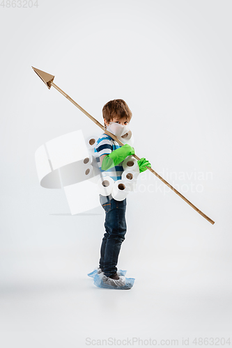 Image of Little caucasian boy as a warrior in fight with coronavirus pandemic, with a face mask, a spear and a toilet paper bandoleer, attacking