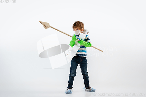 Image of Little caucasian boy as a warrior in fight with coronavirus pandemic, with a face mask, a spear and a toilet paper bandoleer, attacking