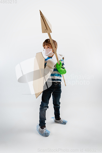 Image of Little caucasian boy as a warrior in fight with coronavirus pandemic, with a shield, a spear and a toilet paper bandoleer, attacking